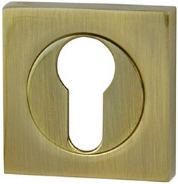 Złota osłona zamka z otworem w kształcie klucza, umieszczona na kwadratowej podstawie.