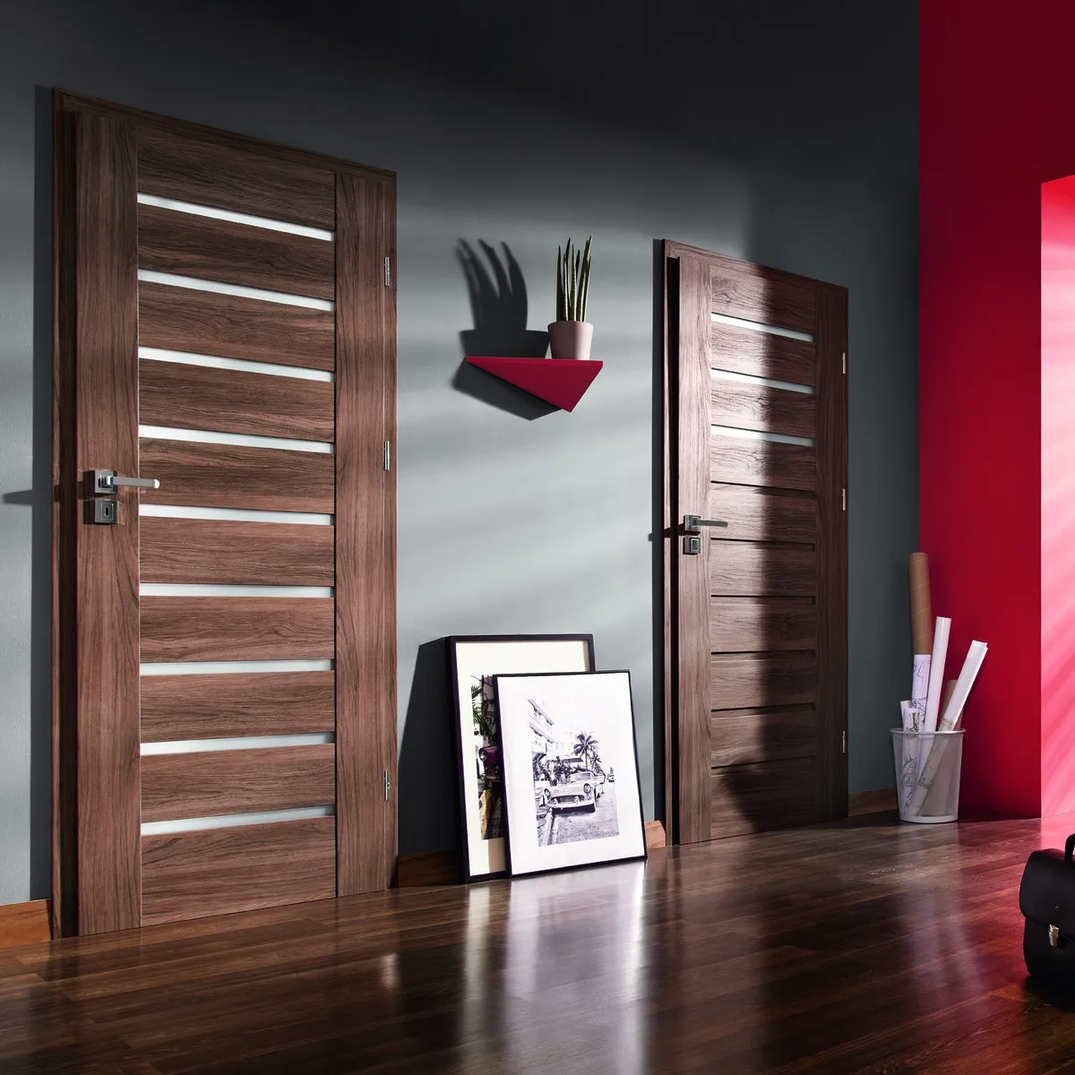 Dwa drewniane drzwi z poziomymi przeszkleniami, obok doniczka z rośliną i ramki ze zdjęciami na podłodze.