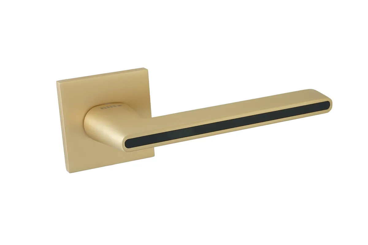 Złota klamka o prostym, nowoczesnym kształcie z czarnym akcentem.